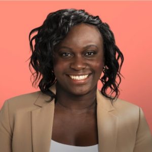 un portrait de Gracia Kasoki Katahwa, une femme noire, qui sourit. Elle porte un blazer beige et un chemise blanc. Le fond est la couleur pêche.