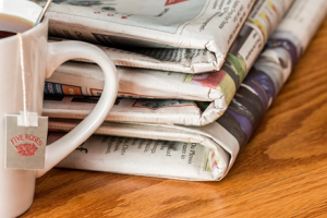 Des journaux et une tasse blanche de thé sur une table en bois